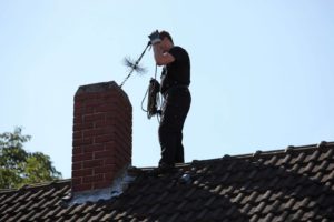 man cleaning chimney on top roof